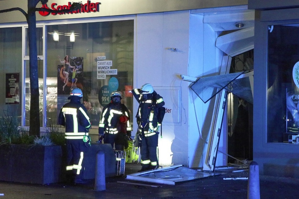 Einsatzkräfte der Feuerwehr stehen vor dem beschädigten Bankgebäude in Langenfeld.