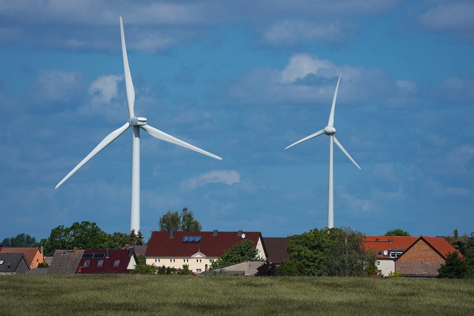 Windräder drehen sich hinter den Häusern des Dorfes. Die Bereitschaft der Menschen, in ihrer unmittelbaren Nähe Windenergieanlagen sowie Stromtrassen zu akzeptieren, ist in Sachsen gering.