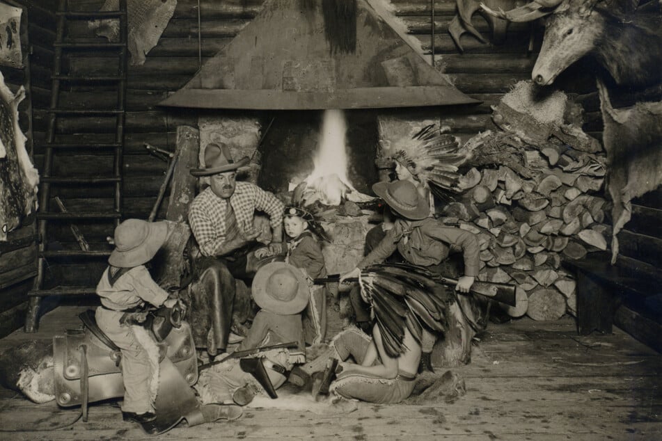 Das historische Foto zeigt Patty Frank inmitten einer Schar kostümierter Kinder im Kamin- oder Trapperzimmer der "Villa Bärenfett".