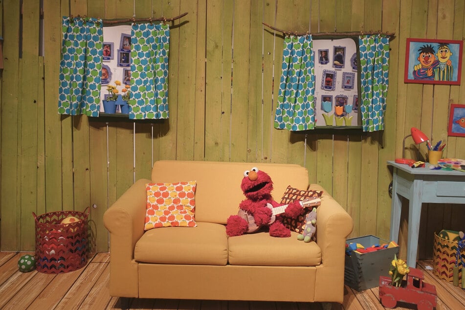 Hier wird eine nachgestellte Kulisse der Sesamstraße gezeigt. Auf dem Sofa sitzt Elmo, das pelzige, rote Monster, das auch aus der amerikanischen Sesame Street stammt und wie die anderen internationalen Stars wie Ernie und Bert, Krümel oder Abby seit 2006 Teil der deutschsprachigen Produktion ist.