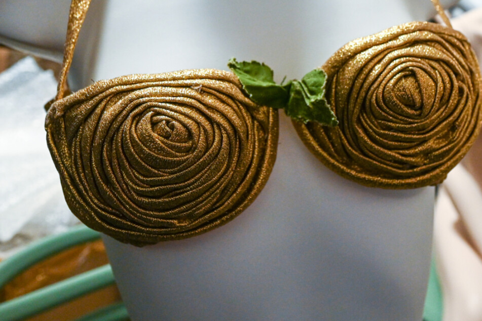 Ein goldener Bikini aus aus der Zeit um 1950 von Louis Réard wird einer Puppe angelegt.