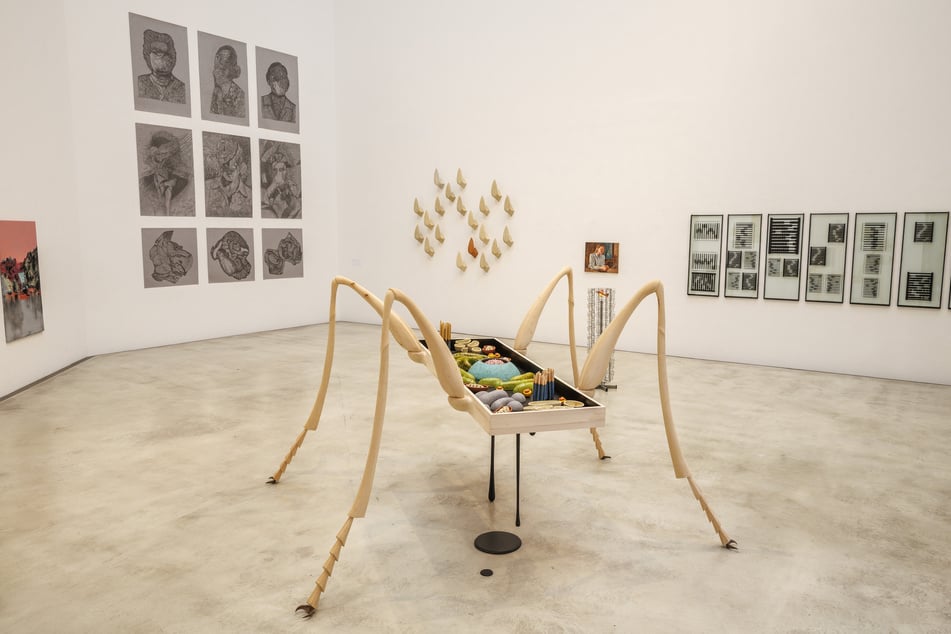 Das an ein Insekt erinnernde Tisch-Objekt "The Arthropod Eukaryote" von Mira Friedrich im Ostragon Ost. Im Hintergrund: Zeichnungen und Collagen von Jupiter Landgraf (l.), die mehrteilige Wandinstallation "An der Oberfläche glänzt es" von Alex Lüder, eines der kleinformatigen Ölgemälde von Antonia Emilie Lehmann (hier: "Sieht keiner hin, ess ich das Glas auf") sowie ganz rechts die Hängung "You shouldn't let poets lie to you" - Werke in Siebdruck und Metall auf Glas von Stefan Kovačević.