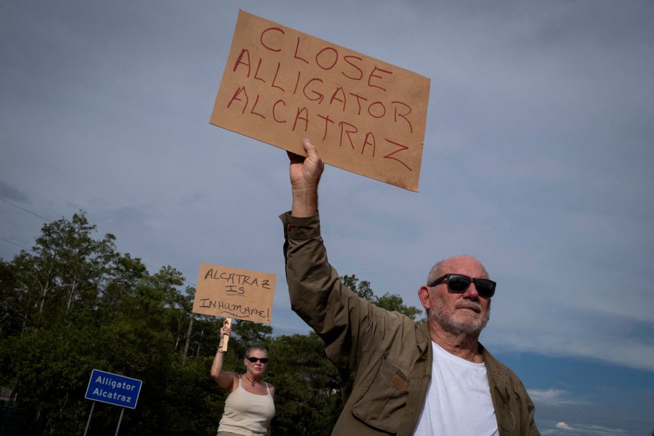 People hold signs calling for the closure of "Alligator Alcatraz" near the entrance to the ICE detention center at the Dade-Collier Training and Transition Airport in Ochopee, Florida.