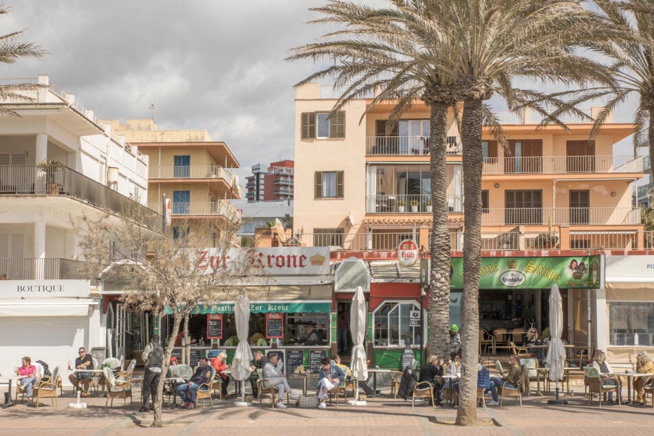 Deutsche Touristen sitzen in der bekannten Bar Zur Krone & Krone Stube und genießen einen Drink in der Sonne an der Playa de Palma auf Mallorca.