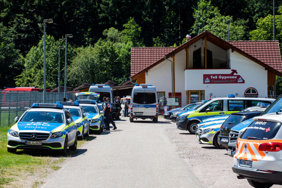 Polizeifahrzeuge stehen auf einem Sammelplatz nahe der Gemeinde vor einem Sportlerheim.