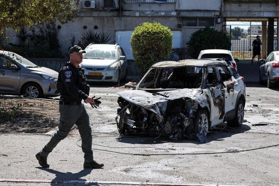 A member of the Israeli Defense Forces walks in font of a charred car near a building hit by a rocket fired from Lebanon in Kiryat Ata in the Haifa district on October 19, 2024.