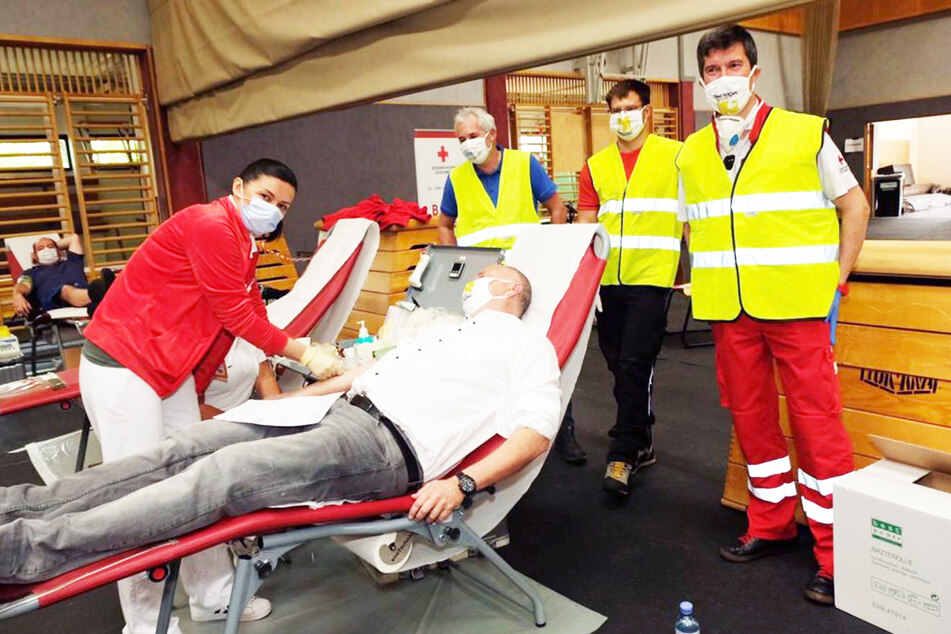 Eine Mitarbeiterin des Blutspendedienstes nimmt einem Spender Blut ab, während die Helfer von Feuerwehr, Bergrettung und Rotem Kreuz zuschauen.