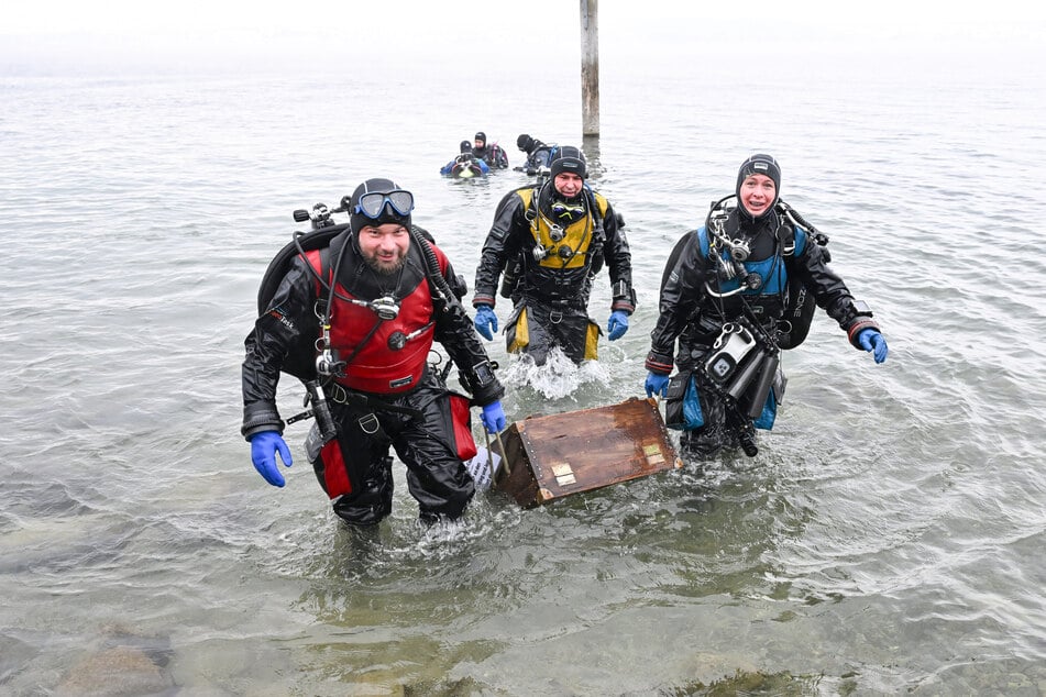 Maren Wagenbreth (a la derecha) y Thomas Wagenbreth del equipo de buceo del Lago de Constanza, y Georg Häußler (a la izquierda) de Archeotask, llevan la caja de madera del tesoro del Lago de Constanza.