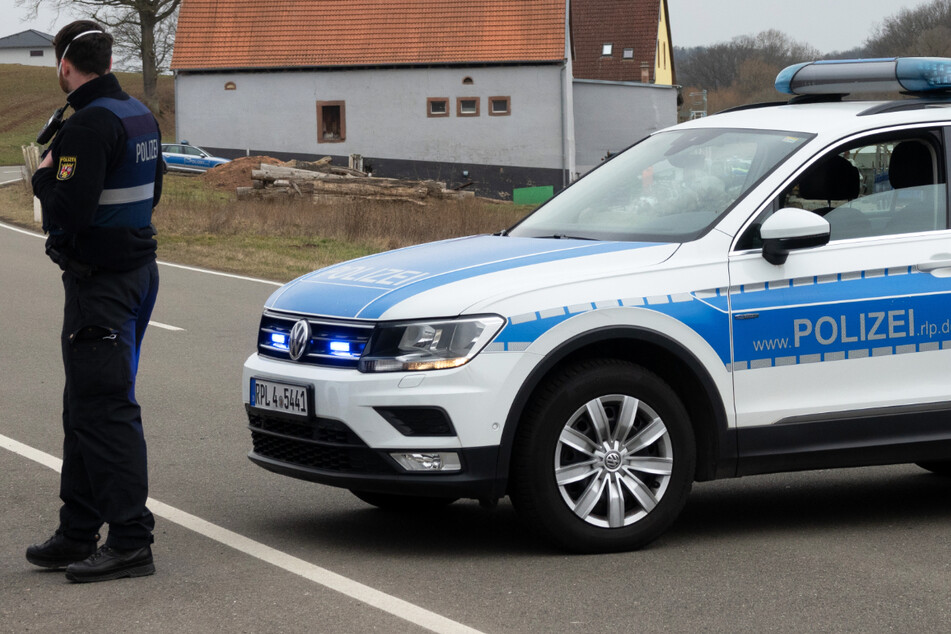 Ein Polizist sperrt mit einem Einsatzfahrzeug eine Straße in Weilerbach bei Kaiserslautern.