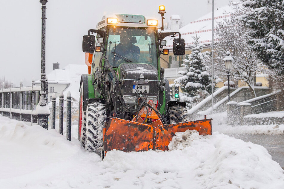 Ein Traktor mit Schneepflug räumt eine verschneite Straße im Ortskern von Tegernsee.
