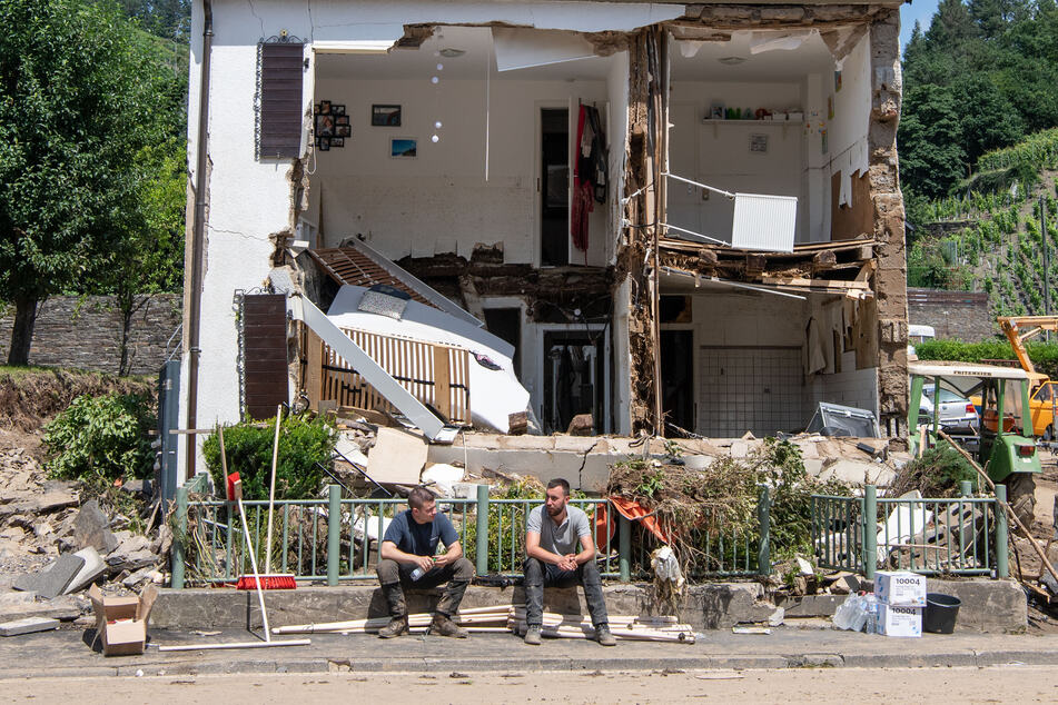 Marienthal, Rheinland-Pfalz: Zwei Männer sitzen vor einem Haus, dessen Fassade von der Flutwelle fortgerissen wurde.