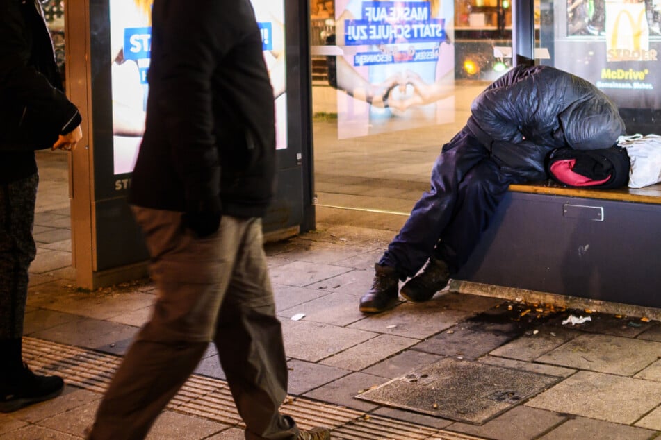 Ein Obdachloser kauert auf der Bank einer Bushaltestelle in Frankfurt am Main.