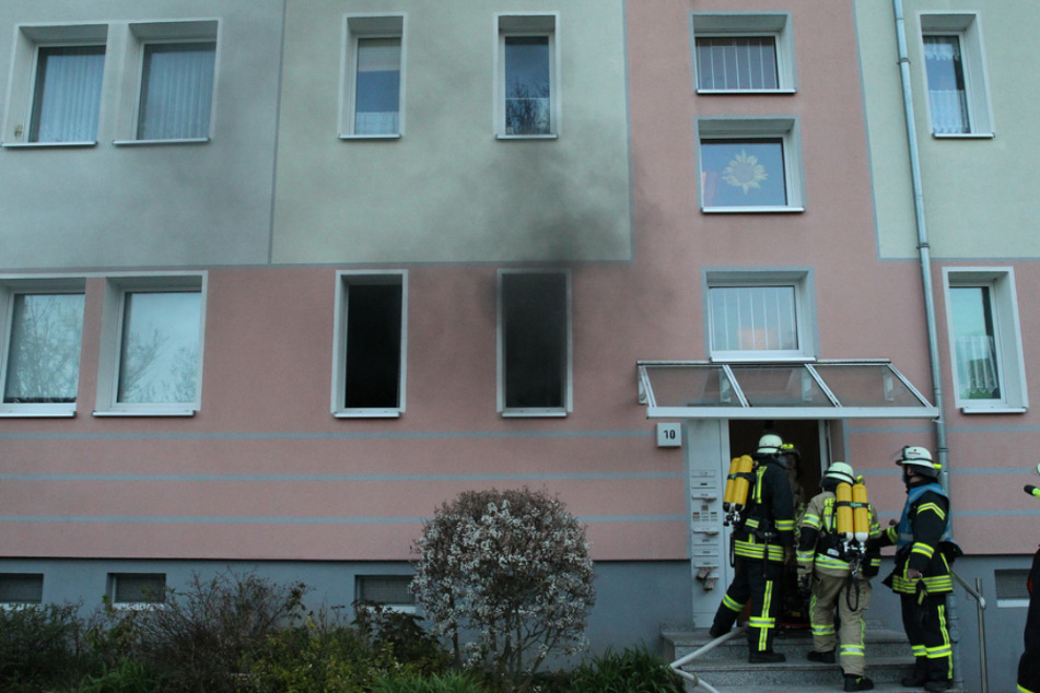 Rauch dringt aus einem Fenster der brennenden Wohnung, während die Feuerwehr das Wohnhaus betritt.