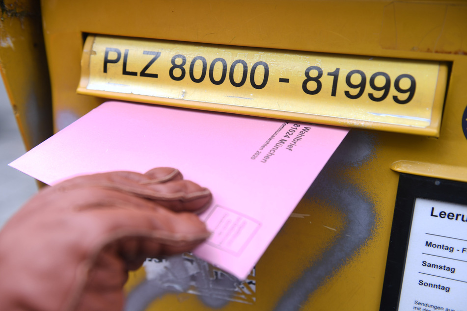 Eine Frau hält die Briefwahlunterlagen für die Kommunalwahl 2020 in der Hand, um diese in einen Briefkasten einzuwerfen.