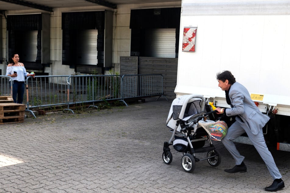 Petrov (Mark Zak, rechts) rettet gerade noch rechtzeitig Tinas (Katja Frenzel) Kinderwagen mit Baby vor dem zurücksetzenden Lastwagen.