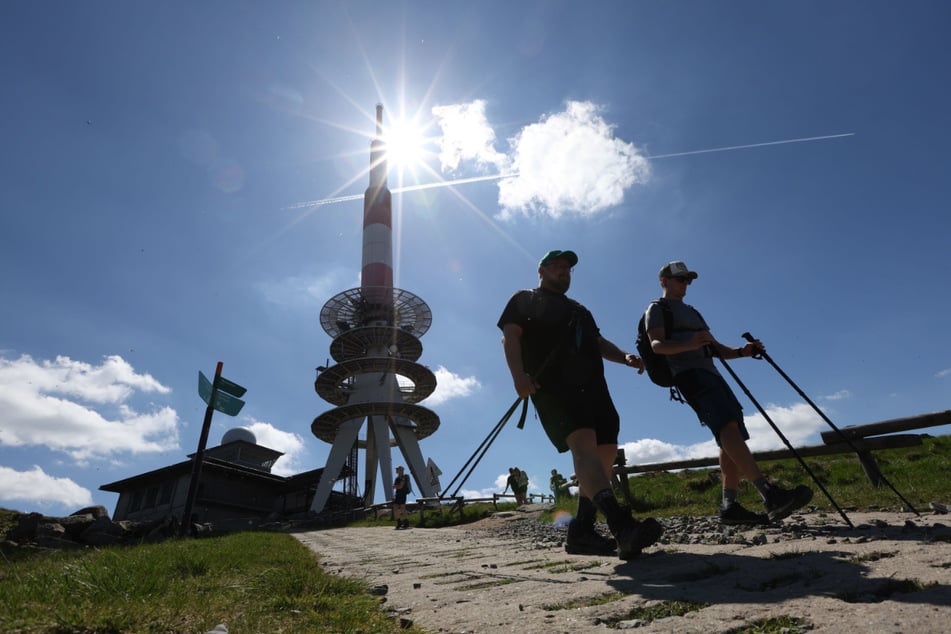 Wanderer gehen bei strahlendem Sonnenschein auf dem Brocken entlang, im Hintergrund steht der Fernmeldeturm.