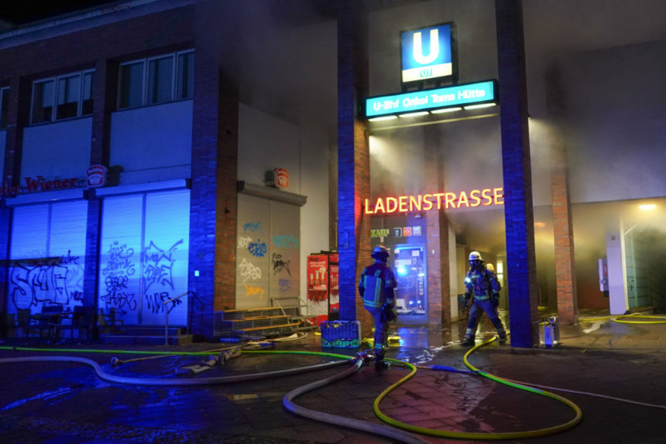 Einsatzkräfte der Feuerwehr löschen einen Brand in der Ladenzeile des U-Bahnhofs Onkel Toms Hütte.