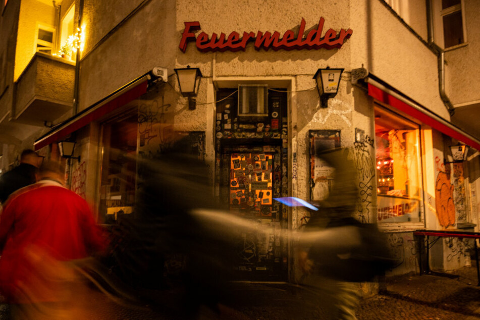 Menschen gehen im Stadtteil Friedrichshain an einer geschlossenen Bar vorbei.