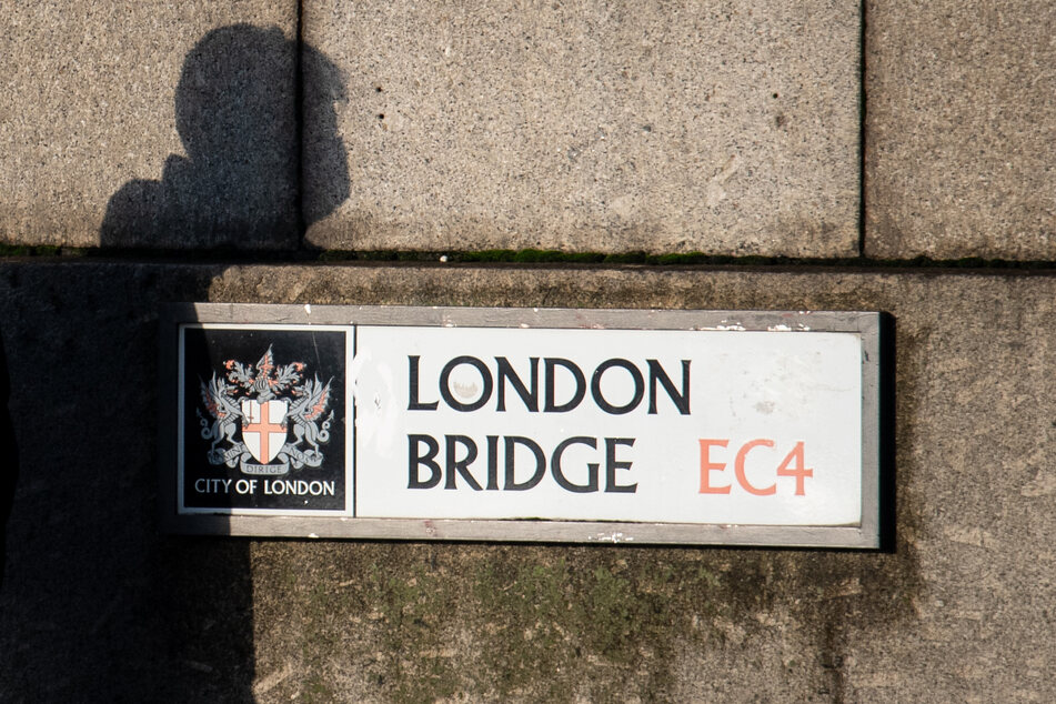 Der Schatten eines Mannes mit einer schützenden Gesichtsmaske ist auf einem Schild auf der London Bridge zu sehen, als Pendler die London Bridge im Zentrum Londons während des morgendlichen Berufsverkehrs überqueren.