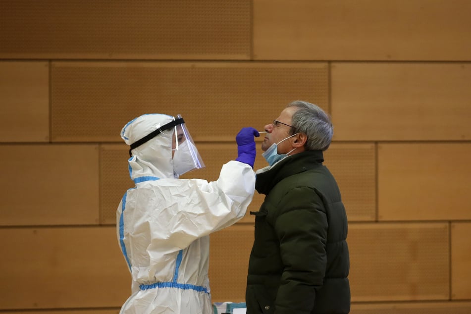 Ein medizinischer Mitarbeiter in Schutzkleidung führt einen Corona-Test an einem Mann durch.