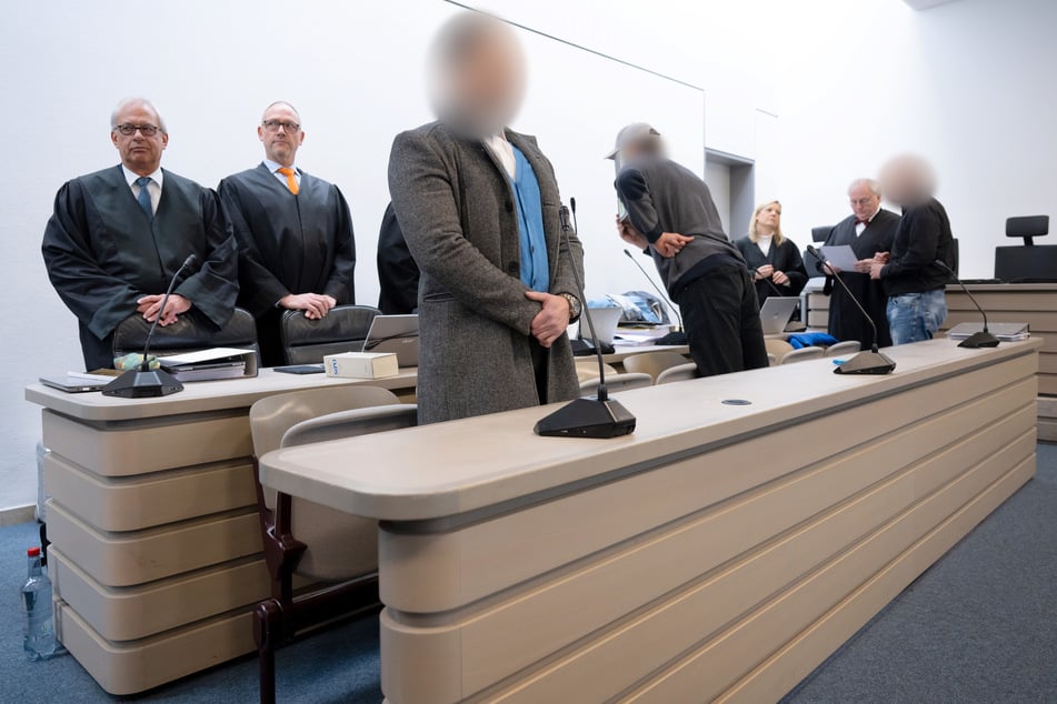 Drei wegen schweren Bandendiebstahls angeklagte Männer (vordere Reihe) stehen vor Prozessbeginn im Gerichtssaal. Insgesamt vier Männer sollen für den Diebstahl eines rund 2100 Jahre alten Goldschatzes im November 2022 aus dem Manchinger Kelten Römer Museum verantwortlich sein.