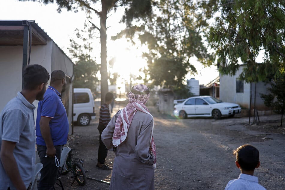 Palestinians stand at the entrance of the Bedouin community of Dar Abu Faza as Israeli settlers pass through with their herd of livestock, on the outskirts of the Israeli-occupied West Bank village of Taybeh, on June 9, 2026.