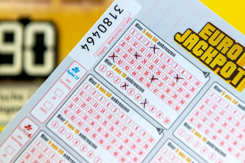 Ein Eurojackpot-Los ist in einer Lotto-Annahmestelle vor einer Tafel zu sehen, auf der auf die Gewinnsumme von 90 Millionen im Eurojackpot hinwiesen wird.