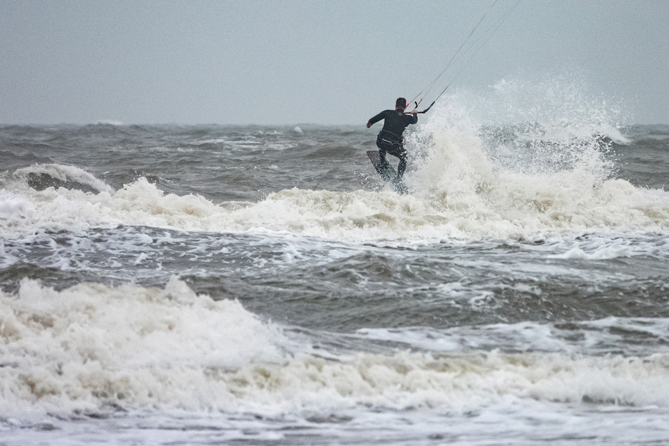 Ein Kitesurfer ist bei stürmischem Wetter und Temperaturen um 14 Grad Celsius auf der rauen Nordsee in St. Peter Ording unterwegs.