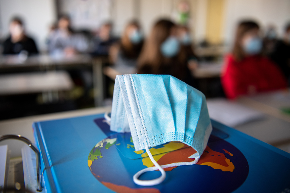Ein Mund- und Nasenschutz liegt in einem Klassenraum. In den Hamburger Schulen werden die Corona-Regeln von Montag an etwas gelockert. (Symbolfoto)