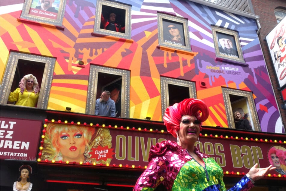 Mit dem Titel "Love-Over-Hate Razzle Dazzle" umrahmt das farbenfrohe Kunstwerk die Fenster, in denen bekannte Gesichter der Olivia-Jones-Familie sowie des Kult-Kieztouren-Teams zu sehen sind.