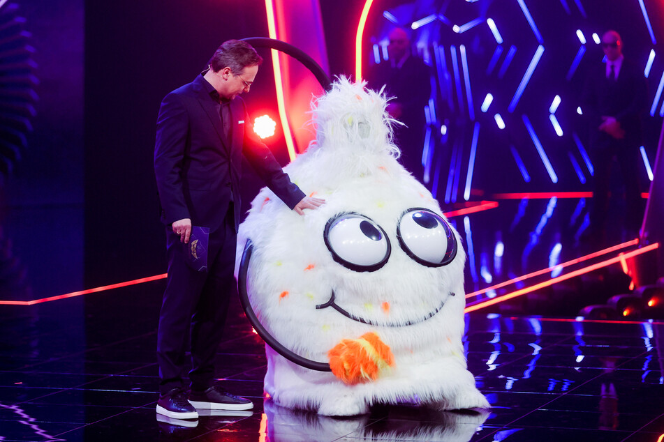 Moderator Matthias Opdenhövel steht neben der Figur "Der Wuschel" in der Prosieben-Show "The Masked Singer" auf der Bühne.