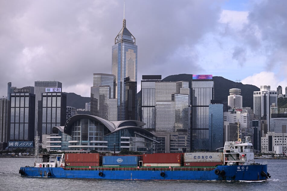 This photo taken on July 1, 2026 shows a ship carrying containers sailing past the Hong Kong skyline in Victoria Harbour, as seen from Kowloon.