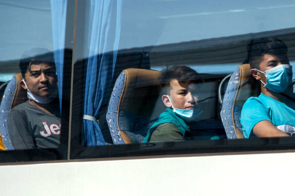 Junge Flüchtlinge, teilweise mit Mundschutz, sitzen in einem Bus am Flughafen Hannover.