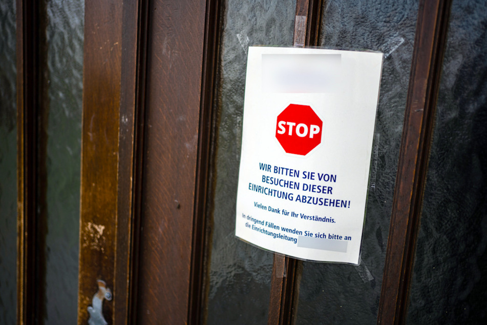 An einer Zugangstür dem Seniorenheim in Würzburg ist ein Schild angebracht, das von Besuchen dieser Einrichtung abrät.