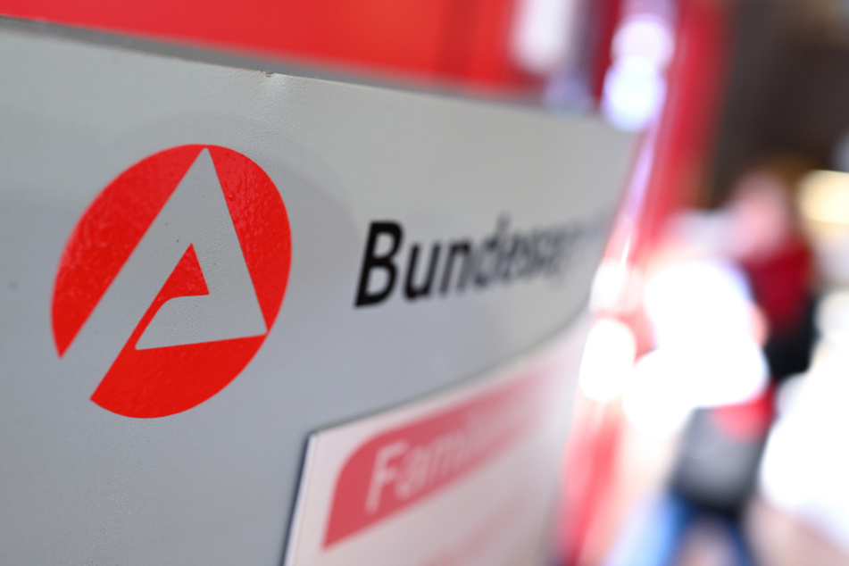 Ravensburg: Auf einer Stele ist das Logo der "Bundesagentur für Arbeit" zu sehen, während im Hintergrund ein Besucher am Informationsschalter steht.