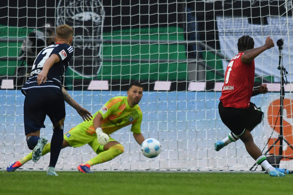 96-Stürmer Jessic Ngankam (r.) verlädt HSV-Keeper Daniel Heuer Fernandes (M.) und trifft vom Punkt zur Führung für die Hausherren.