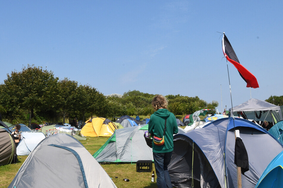 Eine schwarz-rote Flagge einer Antifa-Gruppe weht neben Zelten im Punk-Protestcamp auf der Festwiese bei Tinnum. Bis zum 6. September muss diese geräumt sein.