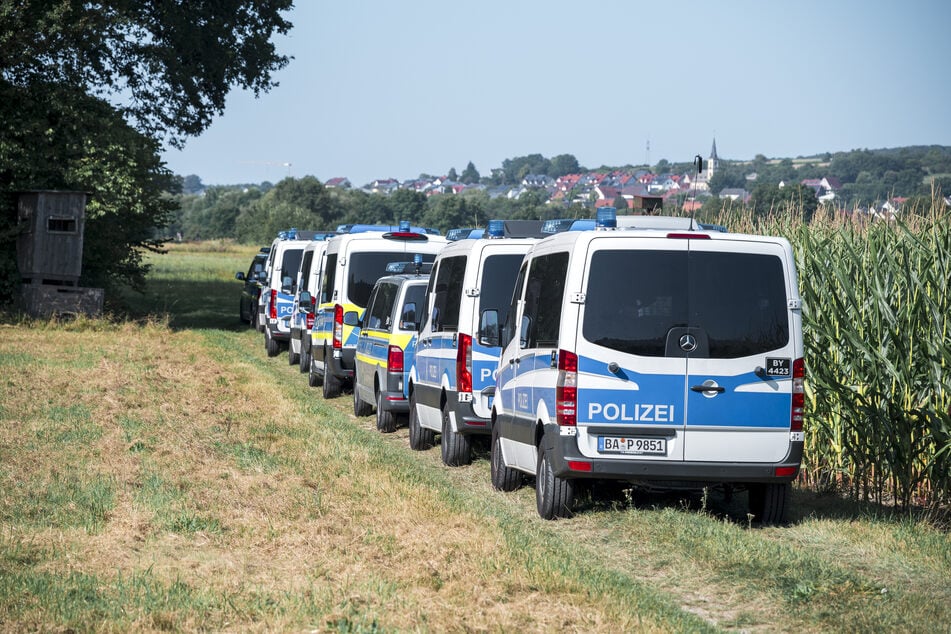 Einsatzfahrzeuge der Bereitschaftspolizei stehen auf einem Feldweg am Waldrand bei Hallerndorf.