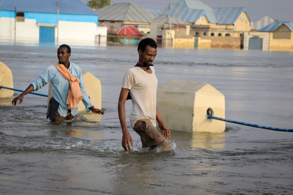 Männer waten durch das Hochwasser auf einer überschwemmten Straße in Beledweyne (Somalia).