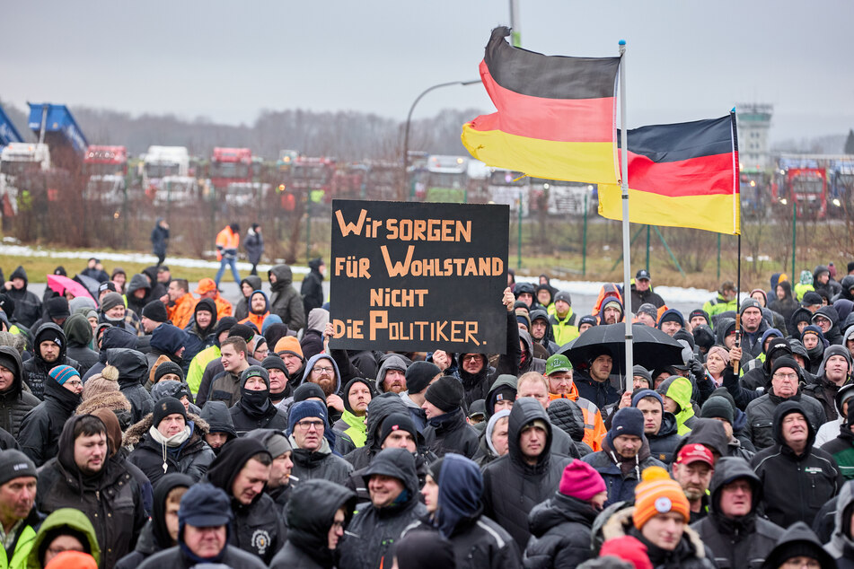 Demonstrierende halten Deutschlandflaggen und ein Transparent mit der Aufschrift "Wir sorgen für Wohlstand, nicht die Politiker" auf dem Flugplatz Hungriger Wolf in die Höhe.