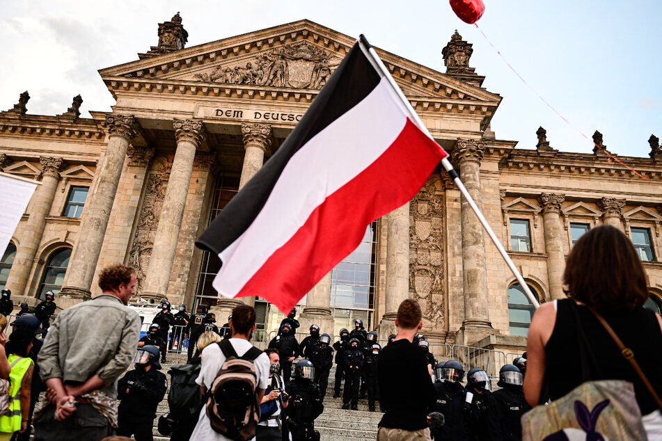 Teilnehmer einer Kundgebung gegen die Corona-Maßnahmen stehen Ende August vor dem Reichstag, ein Teilnehmer hält eine Reichsflagge.