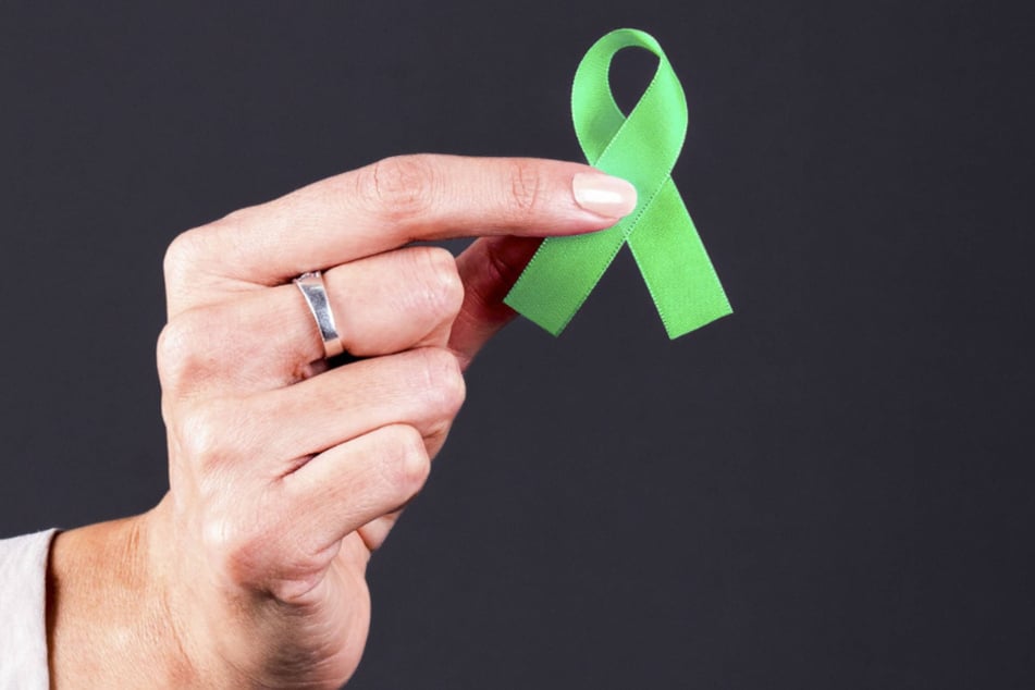 Die Hand einer Frau hält eine grüne Schleife. Diese gilt unter anderem als Symbol für die Bereitschaft zur Organspende.