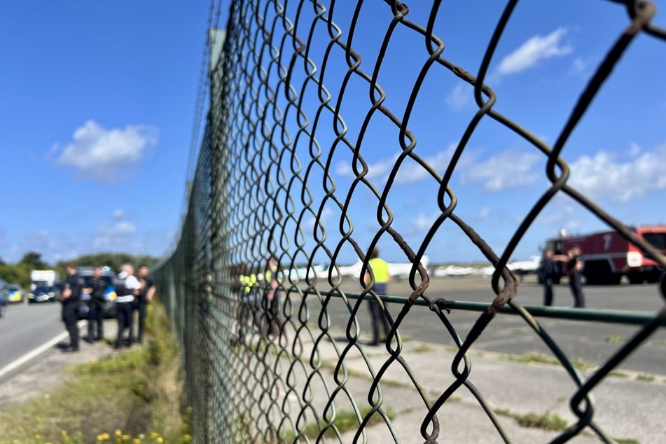 Einsatzkräfte der Polizei und der Feuerwehr stehen am Flughafen. Ein Farbanschlag konnte laut einer Reporterin verhindert werden.