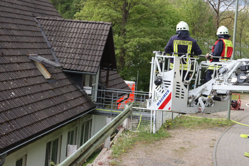 Zwei Feuerwehrleute stehen auf einer Feuerwehrleiter neben dem Dach eines Hauses. Nach dem Löschen eines Wohnungsbrands hat die Feuerwehr in dem Haus in Lennestadt ein lebloses Kleinkind entdeckt.