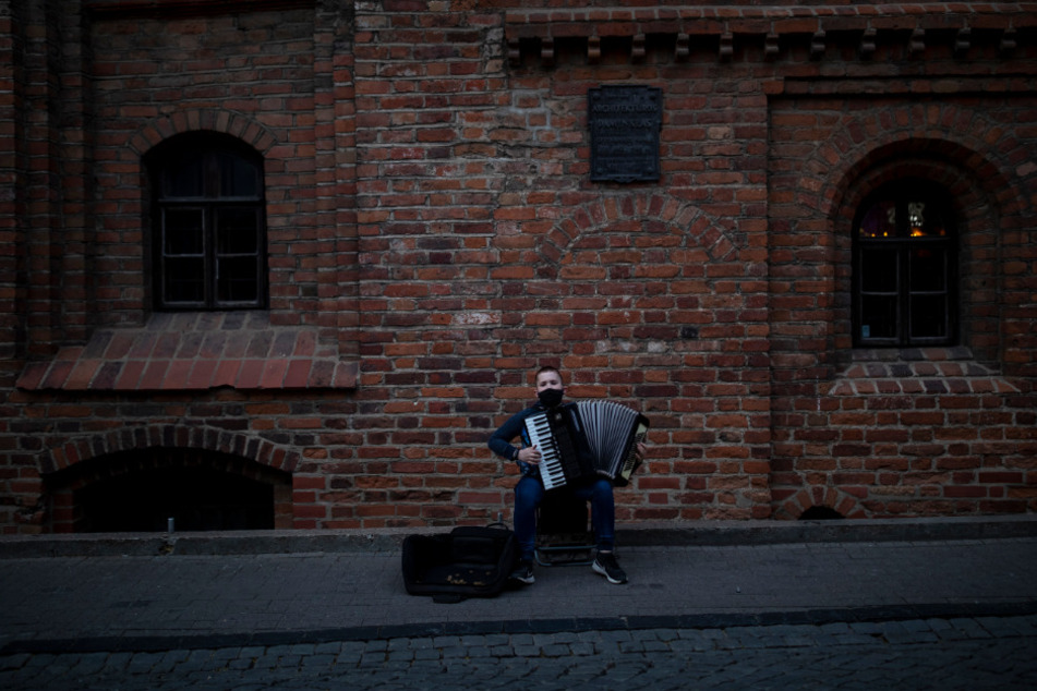 Litauen, Vilnius: Ein junger Straßenmusikant, der zum Schutz vor dem Coronavirus eine Mundschutzmaske trägt, spielt in der Altstadt auf seinem Akkordeon.