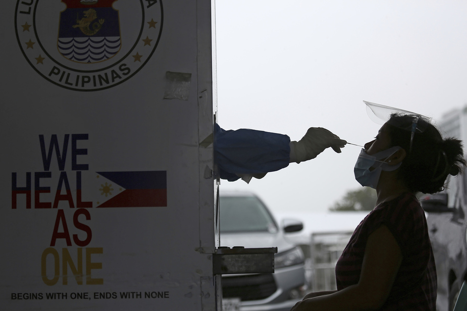 Philippinen, Marikina: Ein medizinischer Mitarbeiter entnimmt an einer Corona-Teststelle eine Abstrichprobe einer Frau für einen Covid-19-Nukleinsäuretest.