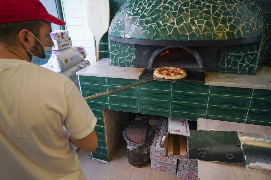 Ein Mann mit Mundschutz nimmt in der Pizzeria Caputo eine Pizza aus dem Ofen.
