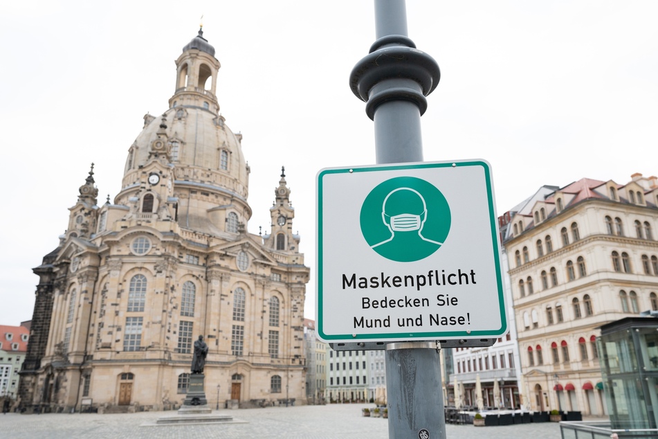 Ein Hinweisschild auf die Maskenpflicht vor der Dresdner Frauenkirche. Diese entfällt nun bei einer Inzidenz unter zehn.