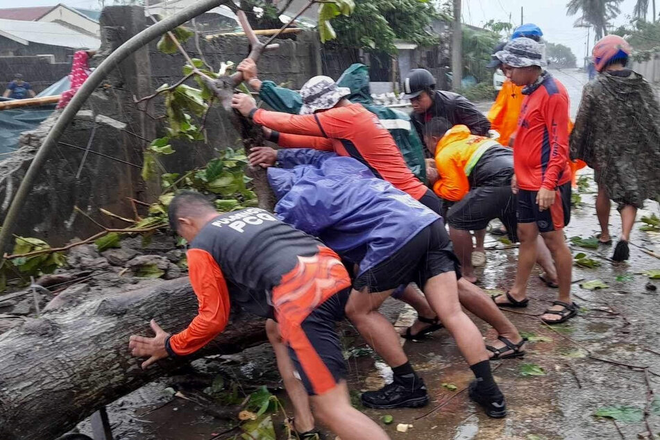 Members of the Philippine Coast Guard remove a fallen tree from a road following the onslaught of Typhoon Doksuri.