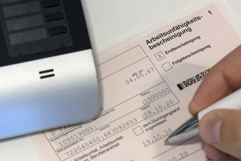 Ein Mitarbeiter einer Arztpraxis notiert etwas auf einer Arbeitsunfähigkeitsbescheinigung (gestellte Szene mit gestellten Daten).